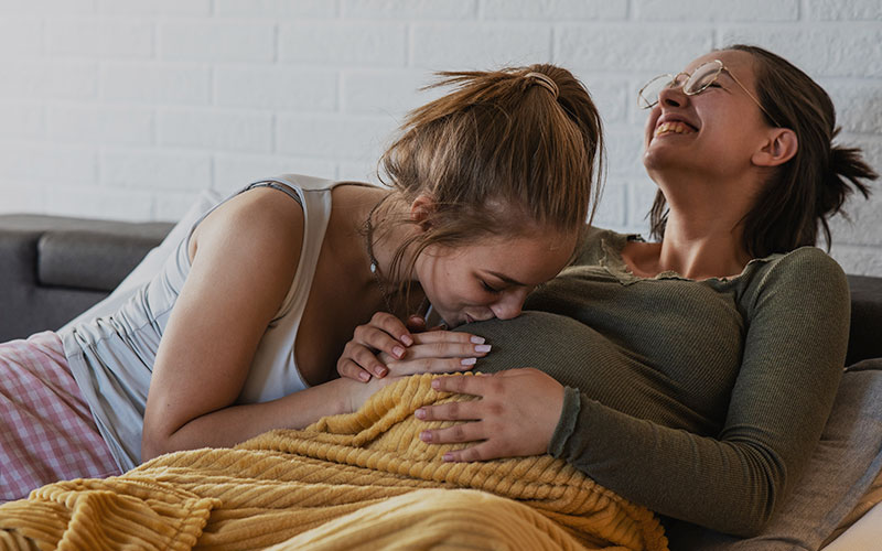 image of lesbian couple with one woman kissing her wife's pregnant stomach